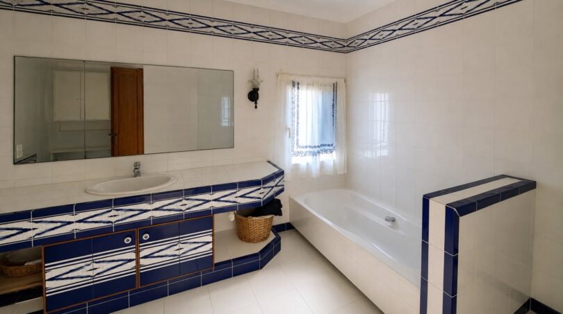 Badezimmer der Finca mit blau-weißen Azulejo-Fliesen, Einbaubadewanne und großem Wandspiegel über dem Waschtisch.