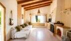Helles Wohnzimmer der Finca mit Holzbalkendecke, weißem Sofa, Gitarre und rustikalem Kamin aus Backstein.