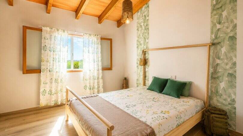 Helles Schlafzimmer der Finca mit Holzbalkendecke, Doppelbett und grünen Akzenten in Lloret de Vistalegre.