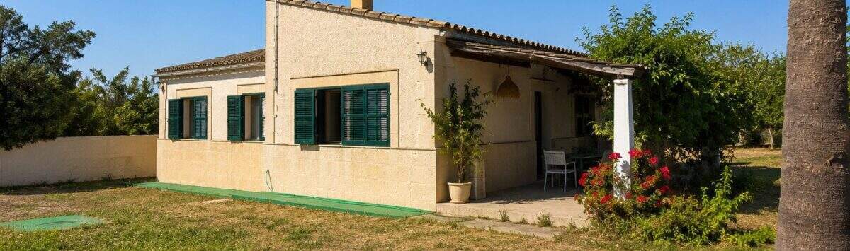 Außenansicht einer mallorquinischen Finca in Lloret de Vistalegre mit grünen Fensterläden und Palme