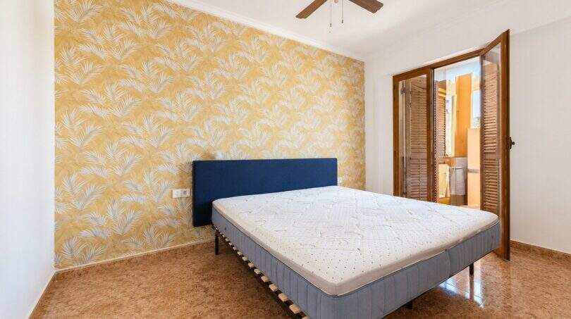 Bedroom with double bed, blue headboard, yellow floral wallpaper accent and ceiling fan in Palma-Camp Redó