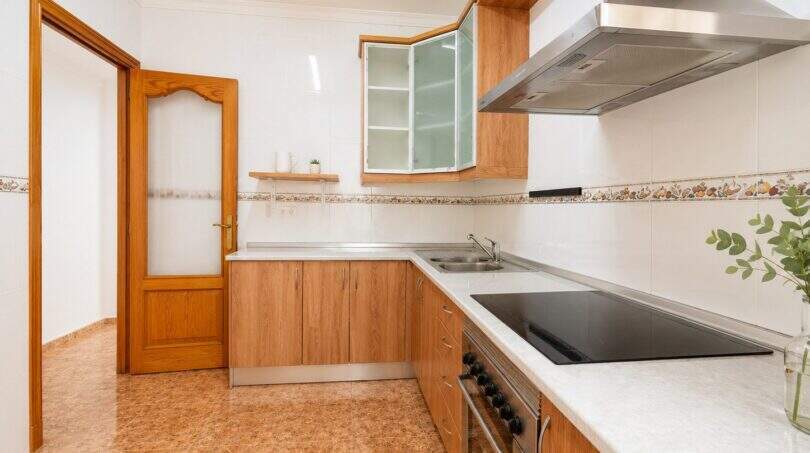 Bright kitchen with wooden fronts, glass ceramic hob, stainless steel hood and tiled walls in apartment in Palma-Camp Redó