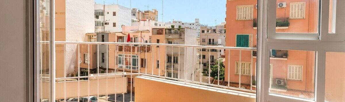 Bright balcony with tiled floor and white railing, view of sunny city buildings in Palma de Mallorca