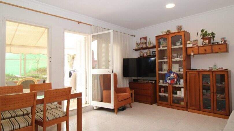 Wohnzimmer des Stadthauses in Portixol mit Esstisch, Holzmöbeln, TV und Zugang zur Terrasse.