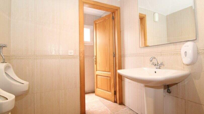 Helles Gäste-WC mit Urinal, Waschbecken, Spiegel und Holztür im Stadthaus Portixol Palma