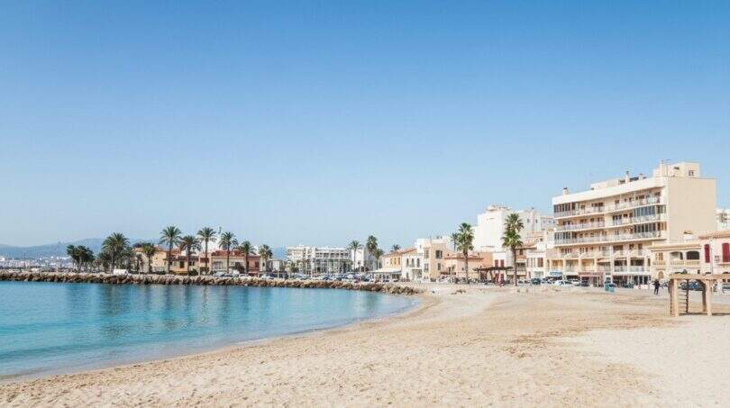 Sandstrand von Portixol mit türkisem Wasser, Palmen und Strandpromenade in Palma de Mallorca