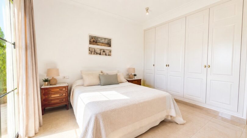 Helles Schlafzimmer der Doppelhaushälfte in Puig de Ros mit Doppelbett, Holznachttischen und weißem Einbauschrank.
