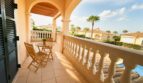 Sonniger Balkon mit Holzmöbeln, Bogenkonstruktion und Blick auf Poolanlage und Palmen in Puig de Ros