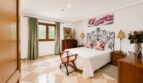Elegantes Schlafzimmer der Finca bei Llucmajor mit schmiedeeisernem Bett, Marmorboden und grünen Vorhängen.