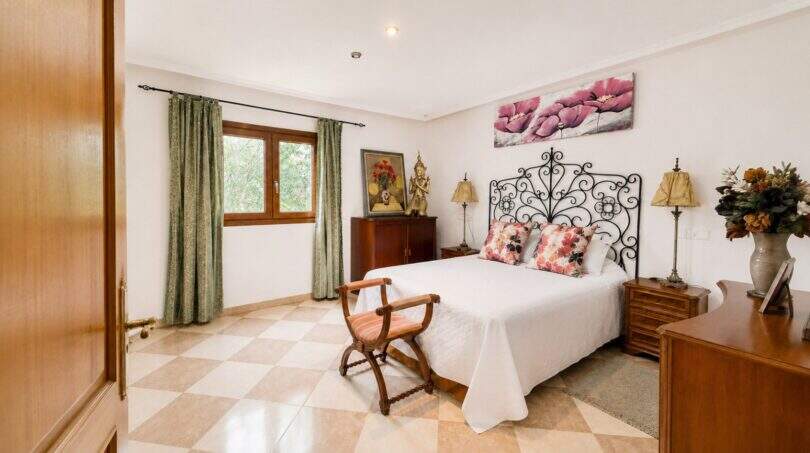 Bedroom of the Llucmajor finca with wrought iron bed, parquet floor and green curtains