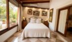 Elegantes Schlafzimmer der Finca Llucmajor mit Doppelbett, Holzbalken, Gemälden und Gartenblick