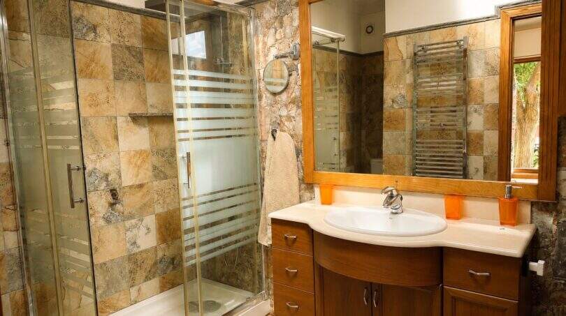 Modern bathroom of the Llucmajor finca with glass shower, natural stone walls and elegant wooden sink