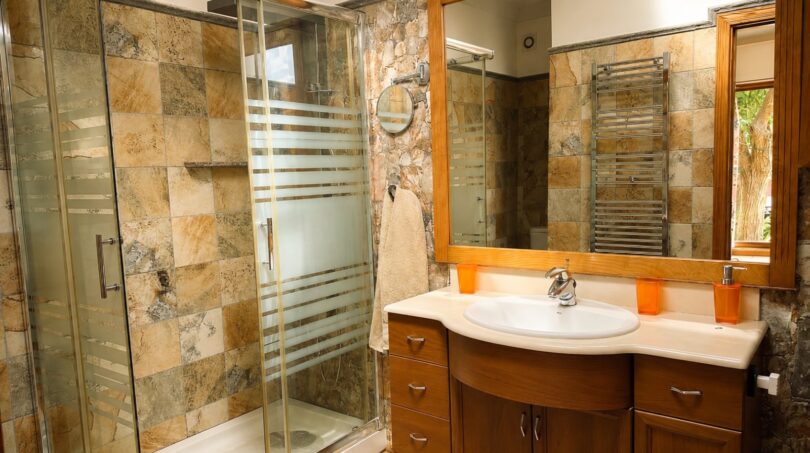 Elegantes Badezimmer der Finca Llucmajor mit Natursteinwänden, Glasdusche und Holzwaschtisch