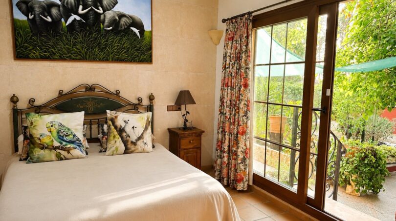Schlafzimmer der Finca Llucmajor mit Schmiedeeisenbett, Elefantengemälde und Balkon mit Gartenblick