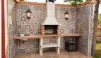 Covered outdoor kitchen of the finca with grill fireplace, mosaic tiles, sink and wall lights