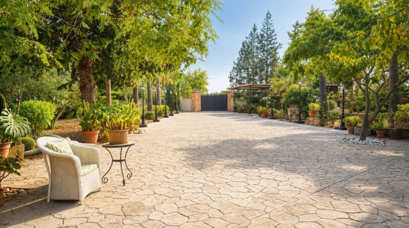 Gepflasterte Einfahrt der Finca Llucmajor mit Gartenanlage, Bäumen, Laternen und schwarzem Eingangstor