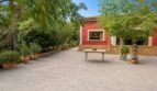 Weitläufige Terrasse der Finca Llucmajor mit roter Fassade, Natursteinmauer und mediterranen Topfpflanzen