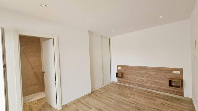 Helles Schlafzimmer mit Holzboden, Einbauschrank, Holz-Kopfteil und angrenzendem Bad in Apartment Cala d'Or