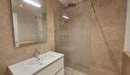 Modernes Badezimmer in Erstbezug-Apartment Cala d'Or mit Walk-in-Dusche, Waschtisch und beigen Fliesen.