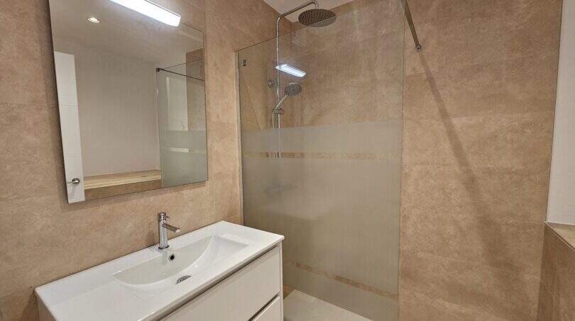 Modernes Badezimmer in Erstbezug-Apartment Cala d'Or mit Walk-in-Dusche, Waschtisch und beigen Fliesen.