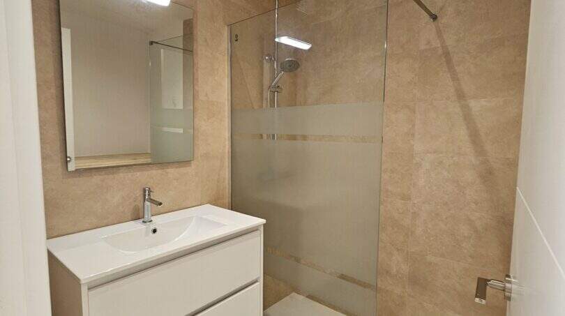 Modernes Badezimmer der Erstbezug-Wohnung in Cala d'Or mit Walk-in-Dusche, schwebendem Waschtisch und Holzoptikboden.