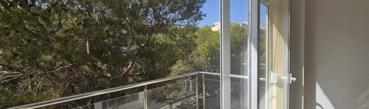 Moderner Balkon mit Glasgeländer und Blick auf grüne Pinien, Wohnung in Palma mit Tiefgarage.