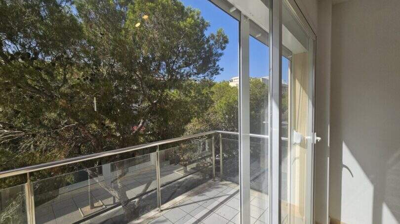 Moderner Balkon mit Glasgeländer und Blick auf grüne Pinien, Wohnung in Palma mit Tiefgarage.
