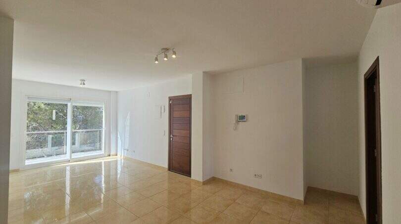 Helles, leeres Wohnzimmer mit Fliesenboden, Balkontür und Holzeingangstür in Wohnung in Palma