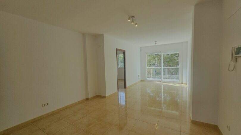 Helles, leeres Wohnzimmer mit Terrakottafliesen, weißen Wänden und Balkontür in Wohnung in Palma