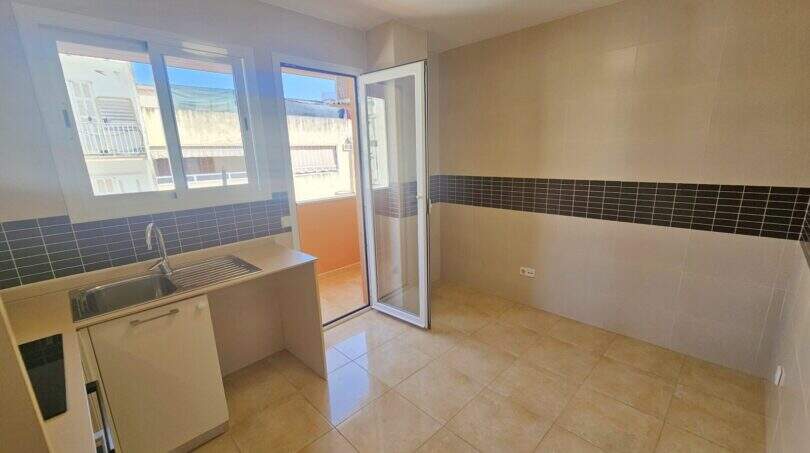 Helle Küche mit Spüle, Fliesenspiegel, Glastür zur Terrasse und großen Fenstern in Palma-Wohnung