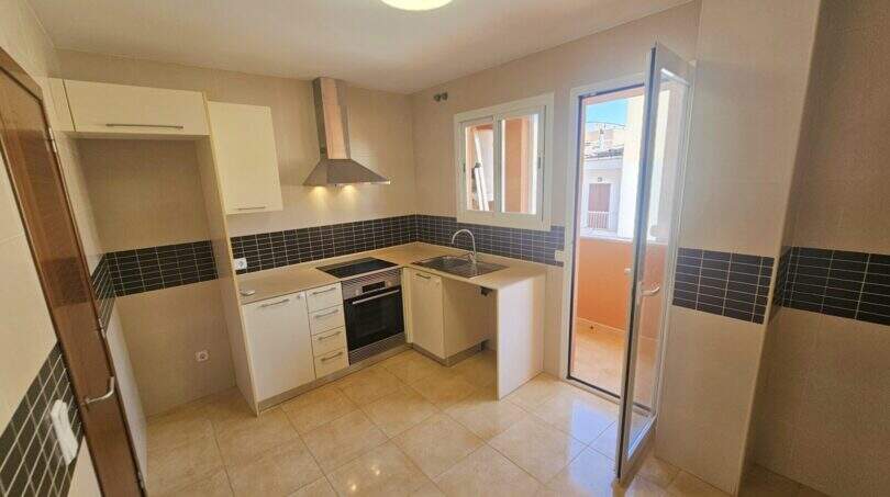 Moderne Einbauküche mit weißen Fronten, Dunstabzug, Backofen und Zugang zur Terrasse in Wohnung Porto Cristo