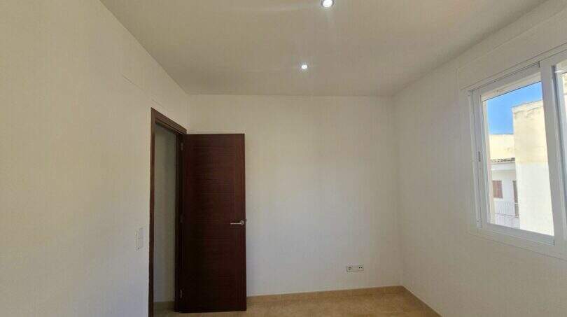 Leeres Schlafzimmer der Wohnung in Porto Cristo mit Fliesenböden, Einbauspot, dunkler Holztür und Fenster.