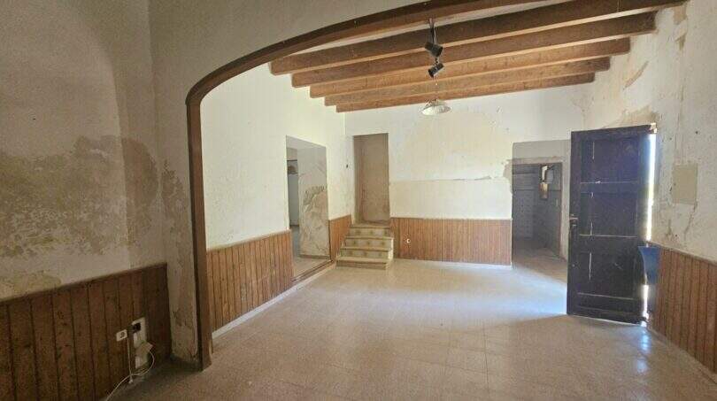 Renovierungsbedürftiger Wohnraum der Finca mit Holzbalkendecke, Rundbogen und Holzverkleidung in Porto Cristo