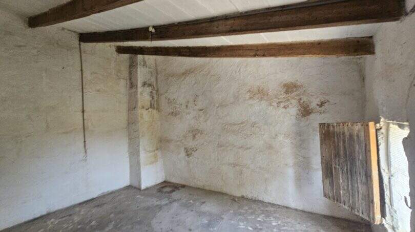 Renovierungsbedürftiger Raum der Finca in Porto Cristo mit rustikalen Holzbalken, Natursteinwänden und Betonboden.