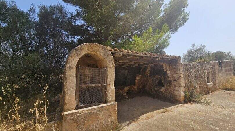 Rustikale Steinmauer mit Rundbogentor und überdachtem Bereich auf renovierungsbedürftiger Finca in Porto Cristo