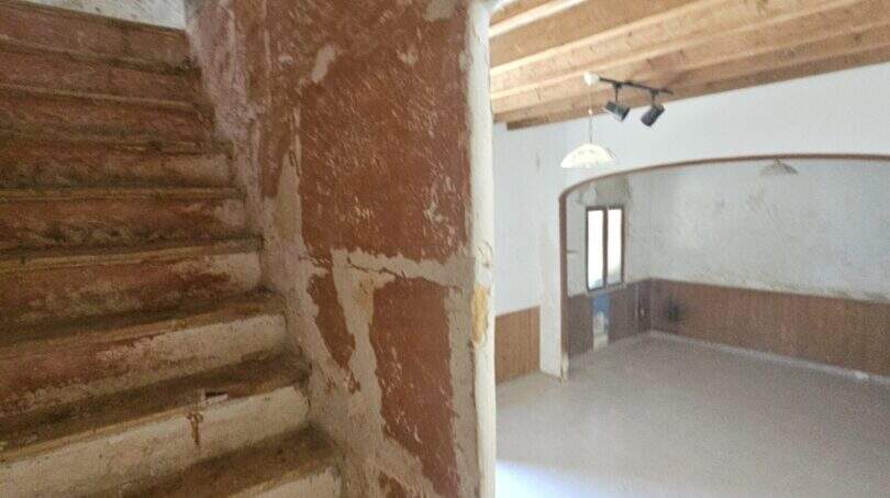 Rustikale Steintreppe und leerer Wohnraum mit Holzbalkendecke und Rundbogen in renovierungsbedürftiger Finca Porto Cristo