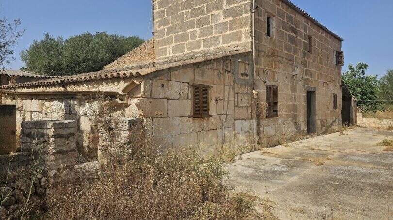 Außenansicht renovierungsbedürftige Finca Porto Cristo: historisches Sandsteingebäude mit Nebengebäuden und weitläufigem Grundstück.