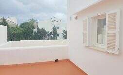 Sonnige Dachterrasse mit weißem Geländer, Fensterläden und Blick auf Bäume und Nachbargebäude in Cala d'Or