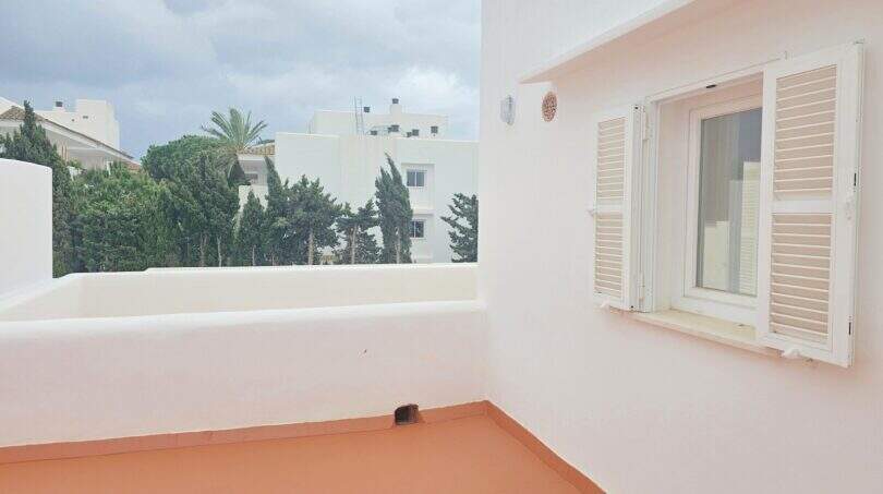 Sonnige Dachterrasse mit weißem Geländer, Fensterläden und Blick auf Bäume und Nachbargebäude in Cala d'Or