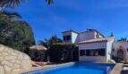 Außenansicht: Mediterranes Ferienhaus in Cala Romántica mit blauem Pool, Sonnenterrasse und üppigem Grün unter strahlend blauem Himmel.