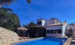 Exterior view: Mediterranean holiday home in Cala Romántica with blue pool, sun terrace and lush greenery under a bright blue sky.
