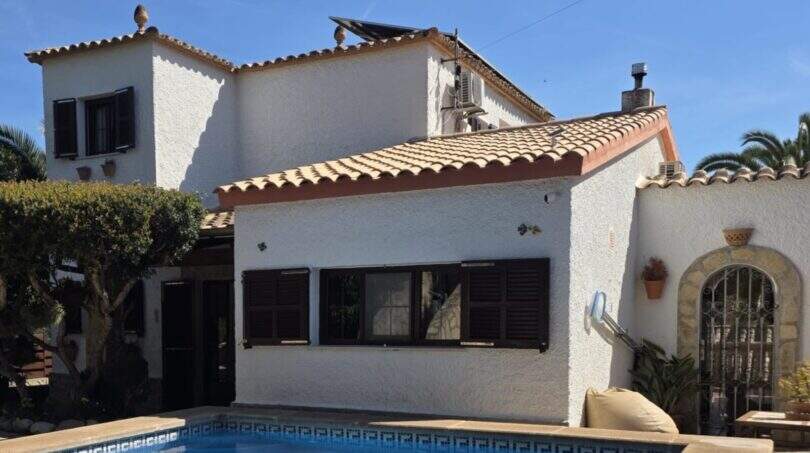 Außenansicht Villa Porto Cristo Novo: weißes Mediterranhaus mit Terrakotta-Ziegeldach, braunen Fensterläden und blauem Pool.