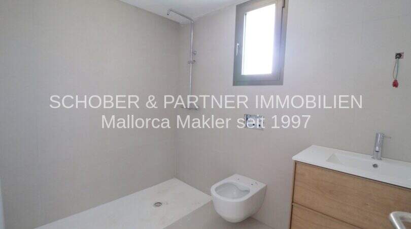 Moderno baño con ducha a nivel del suelo, inodoro de pared y lavabo de madera en el apartamento de nueva construcción Cala Millor