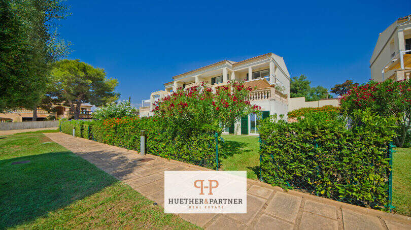 Außenansicht Reiheneckhaus Porto Cristo Novo, gepflegter Garten mit Hecken, Balkon und rotem Oleander, blauer Himmel.
