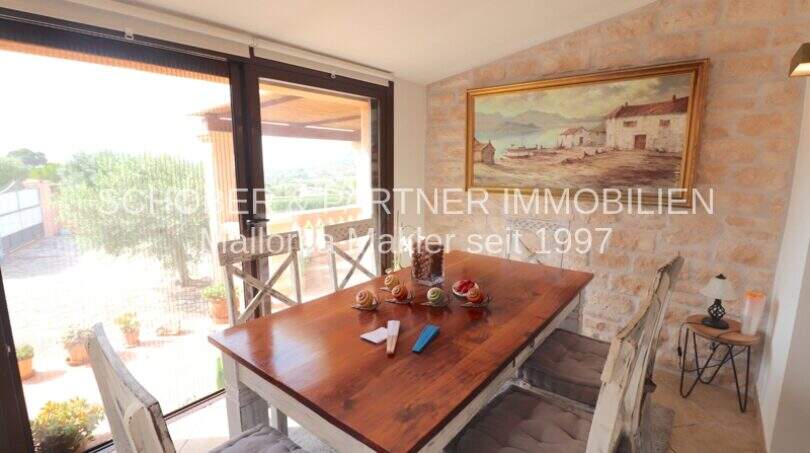 Bright dining room with wooden table, natural stone wall and large glass front with panoramic view in Son Servera
