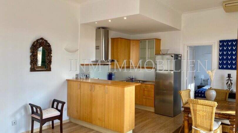 Cocina abierta con frentes de madera y frigorífico de acero inoxidable, zona de comedor adyacente en apartamento del casco antiguo de Palma
