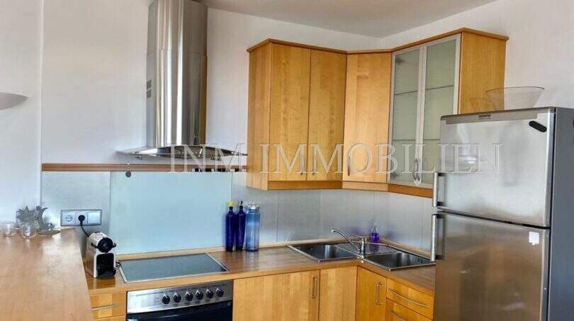 Cocina empotrada moderna con frentes de madera, campana de acero inoxidable, vitrocerámica y frigorífico en apartamento del casco antiguo de Palma
