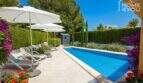Sonniger Poolbereich mit Liegestühlen, Sonnenschirmen und blühenden Bougainvilleen im gepflegten Garten des Bungalows in Alcúdia.