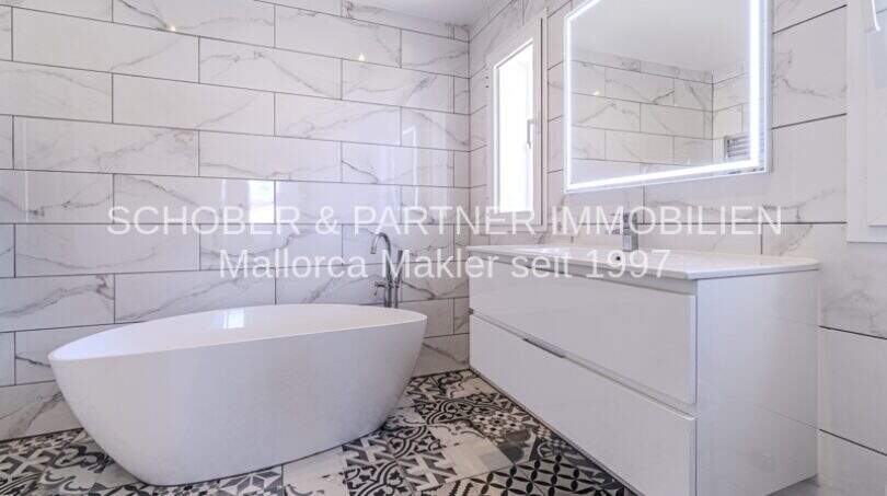 Elegantes Badezimmer mit freistehender Badewanne, Marmorfliesen und modernem Waschtisch in mediterraner Villa Sa Coma