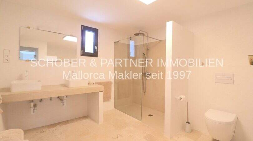 Helles Badezimmer mit Doppelwaschbecken, ebenerdiger Glasdusche und WC im sanierten Landhaus in Portocristo